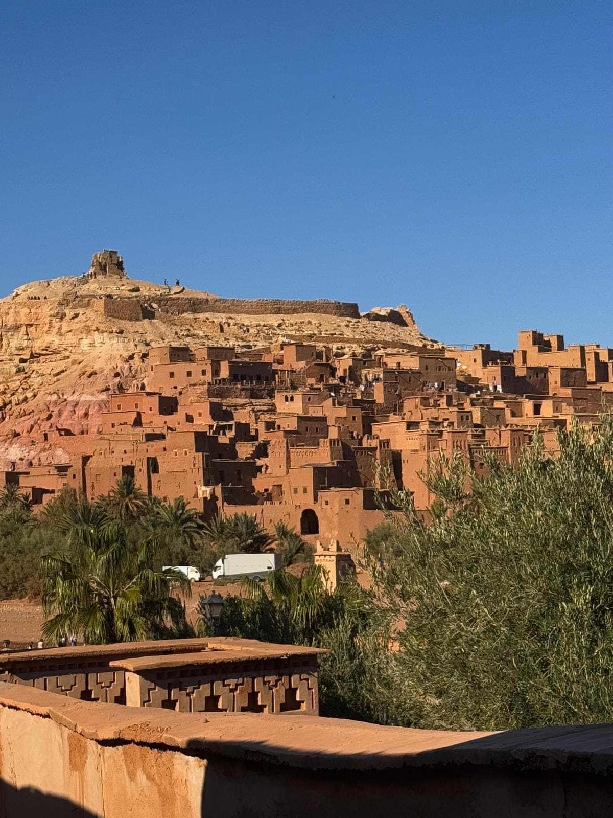 De lemen huizen van de ksar van Aït Benhaddou op de heuvel, met palmen ervoor