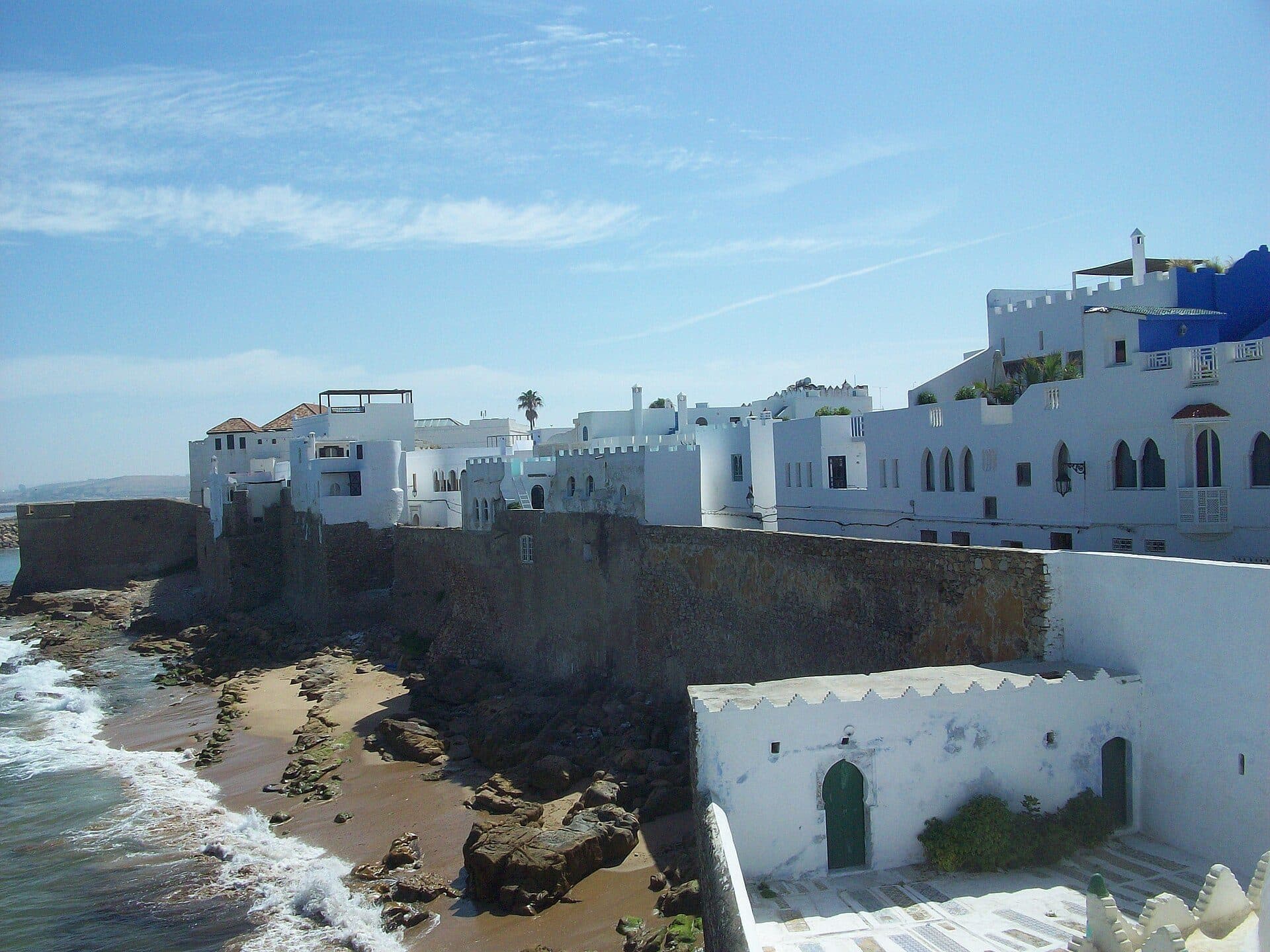 Witte huizen boven de oude stadsmuur van Asilah, met een strandje en golven aan de voet