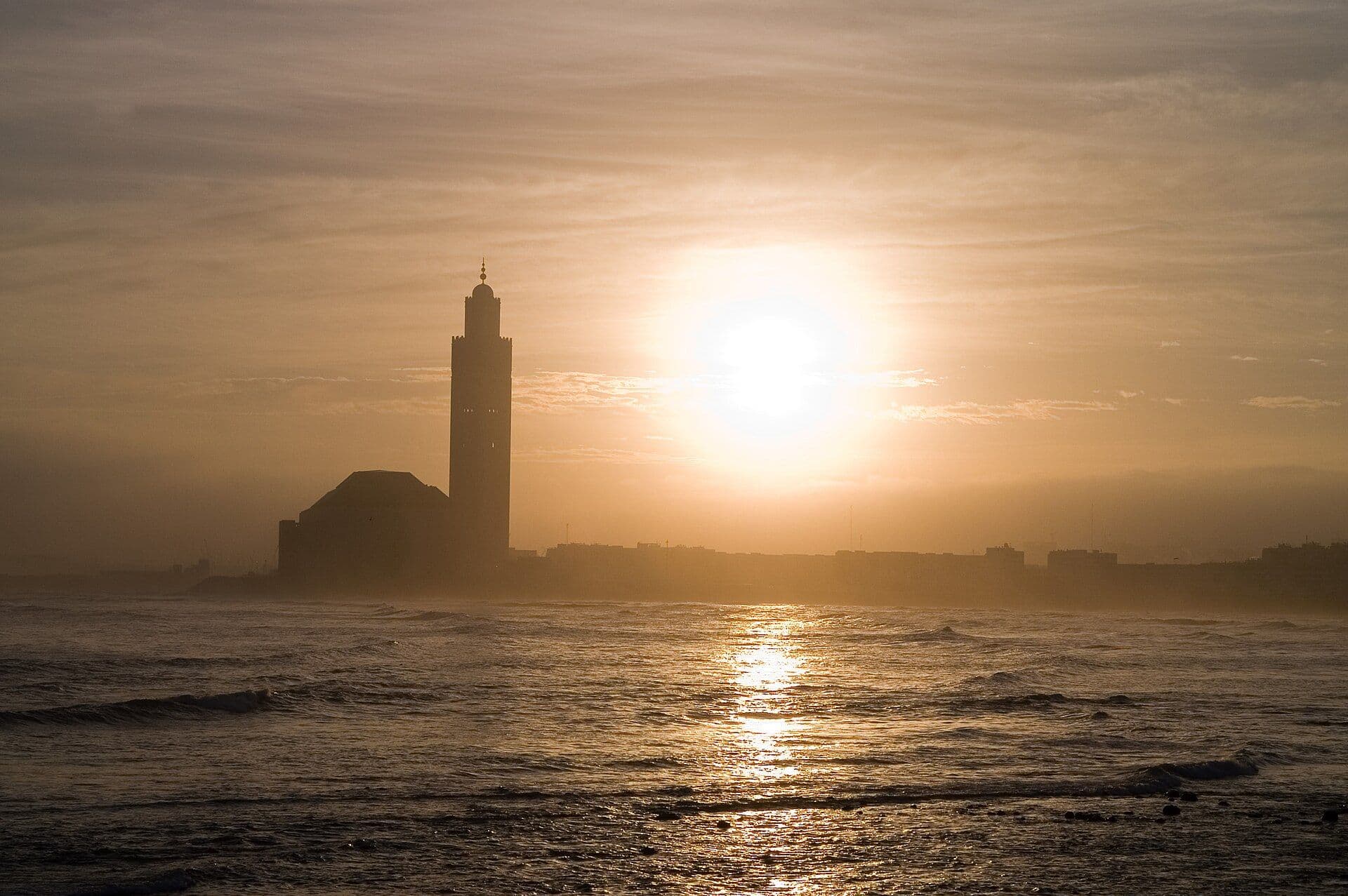 Het silhouet van de Hassan II-moskee in Casablanca tegen de zonsondergang boven de oceaan