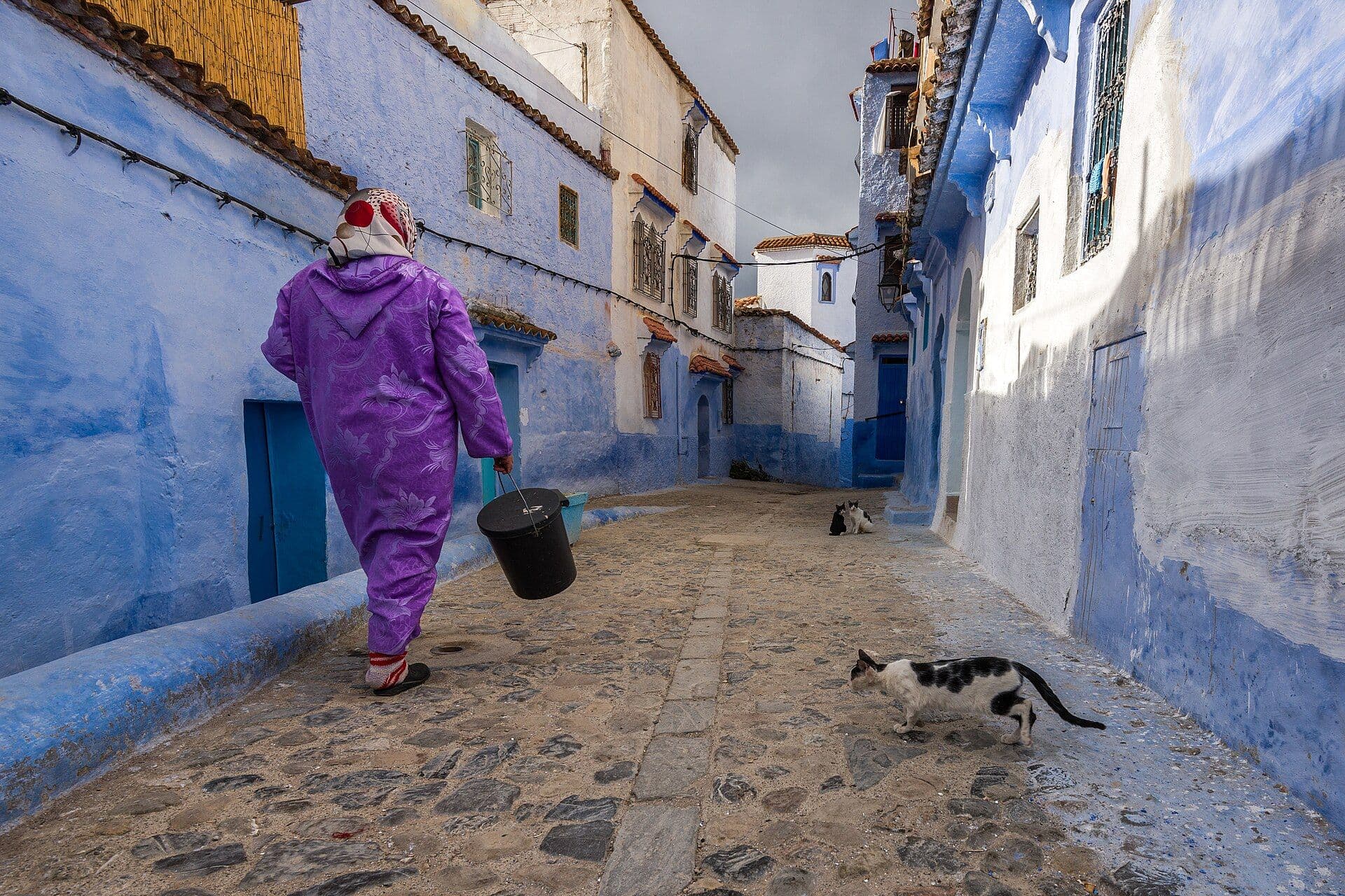 Vrouw in paarse djellaba loopt door een blauwe steeg in Chefchaouen