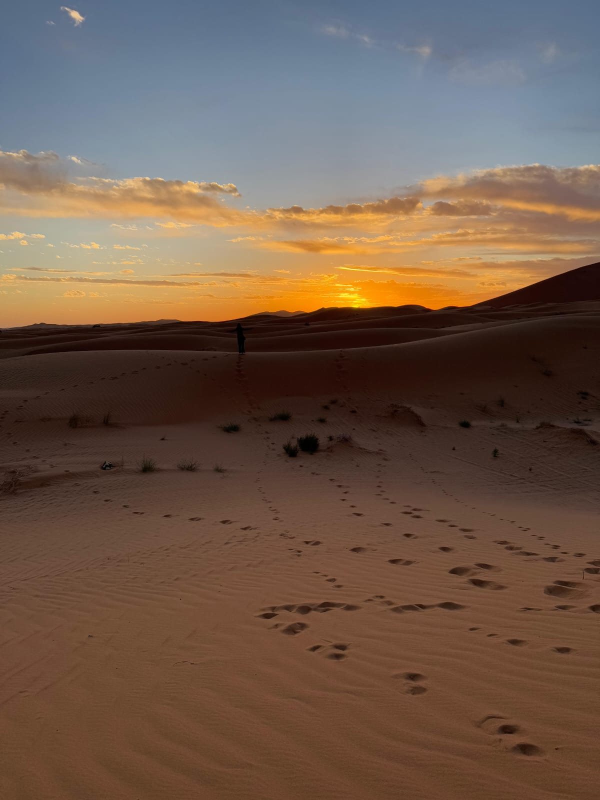 De zon gaat onder achter de duinen van Erg Chebbi bij Merzouga, met voetsporen in het zand
