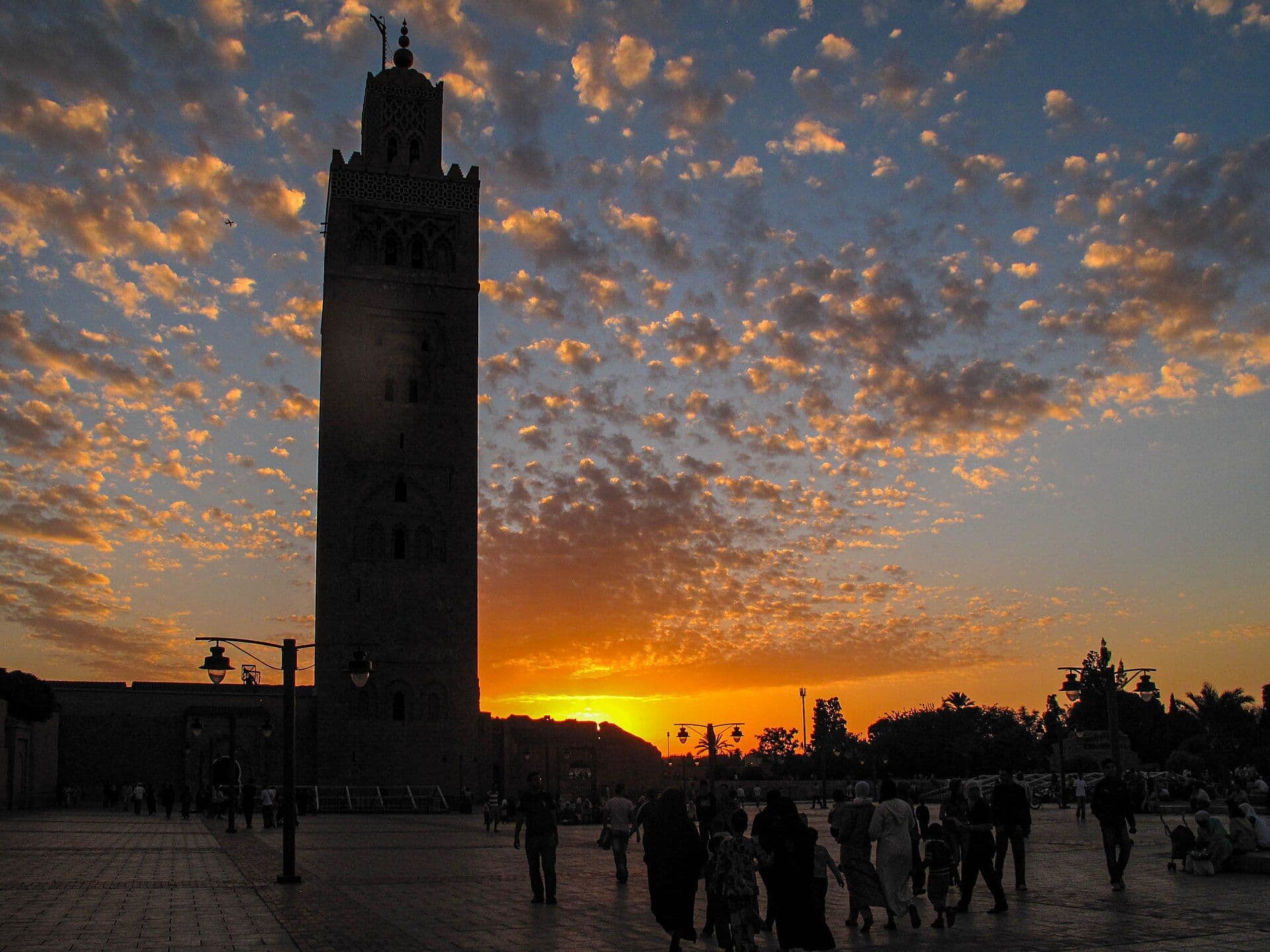 De Koutoubia-moskee in Marrakesh bij zonsondergang, met wandelaars op het plein ervoor