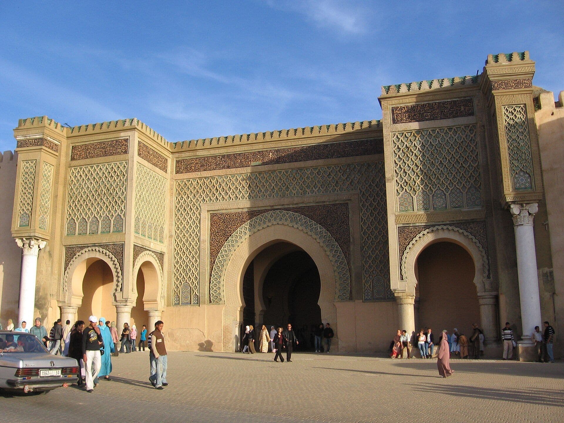 De grote versierde poort Bab Mansour in Meknès met mensen op het plein ervoor