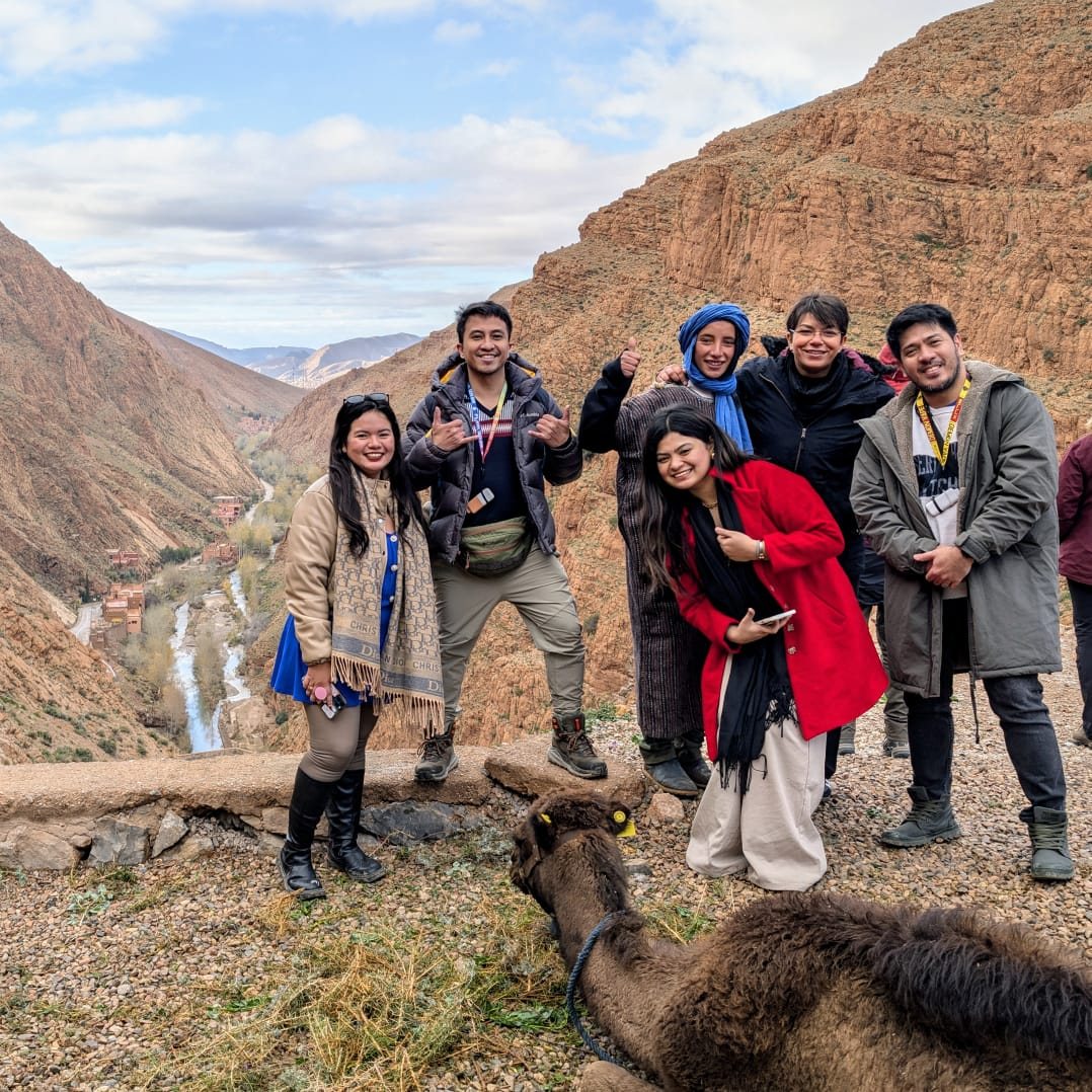 Een groep reizigers lacht naar de camera boven de Dadès-kloof, met de rivier diep beneden