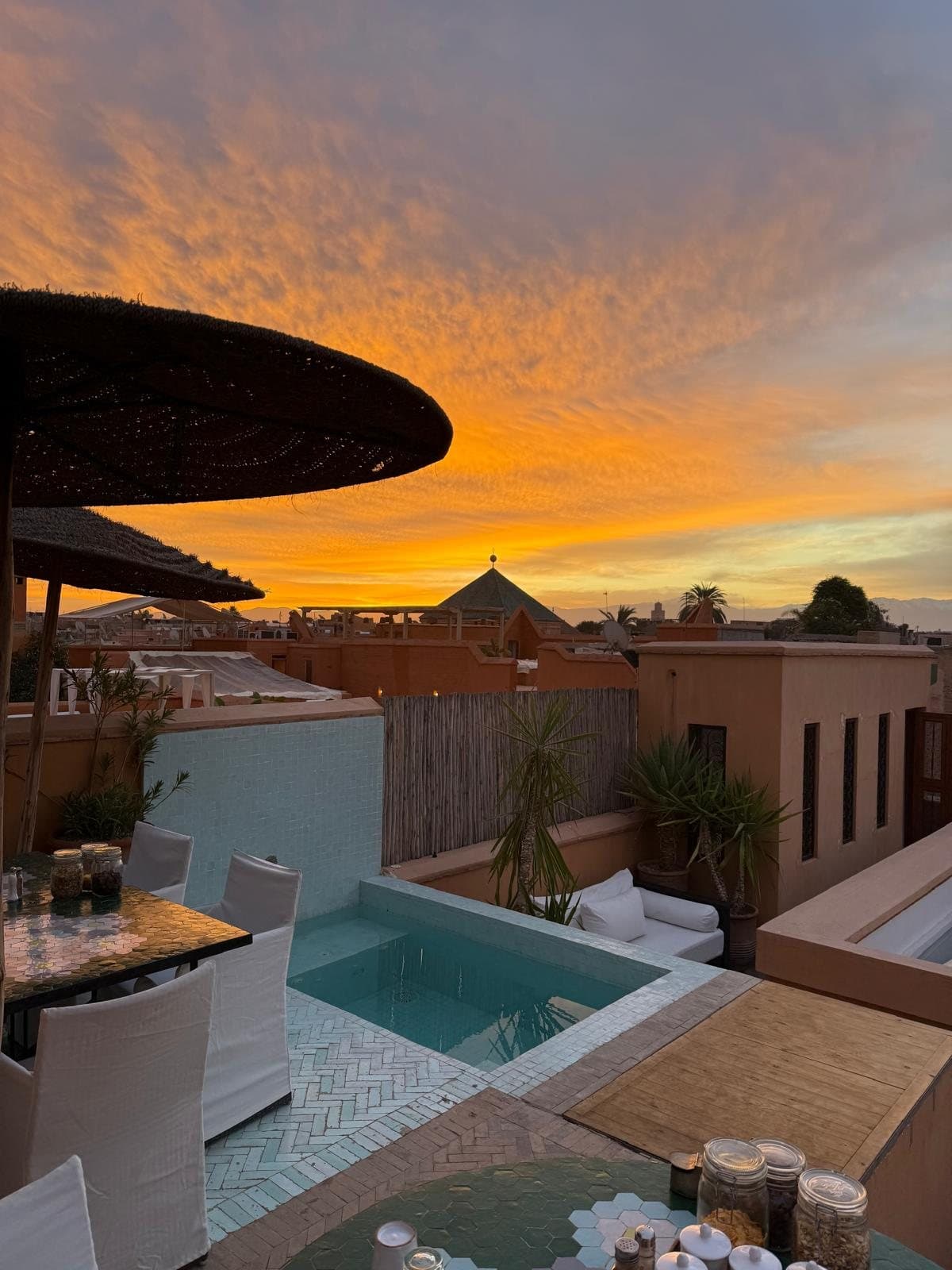 Een dakterras met een klein zwembad en parasols bij zonsondergang