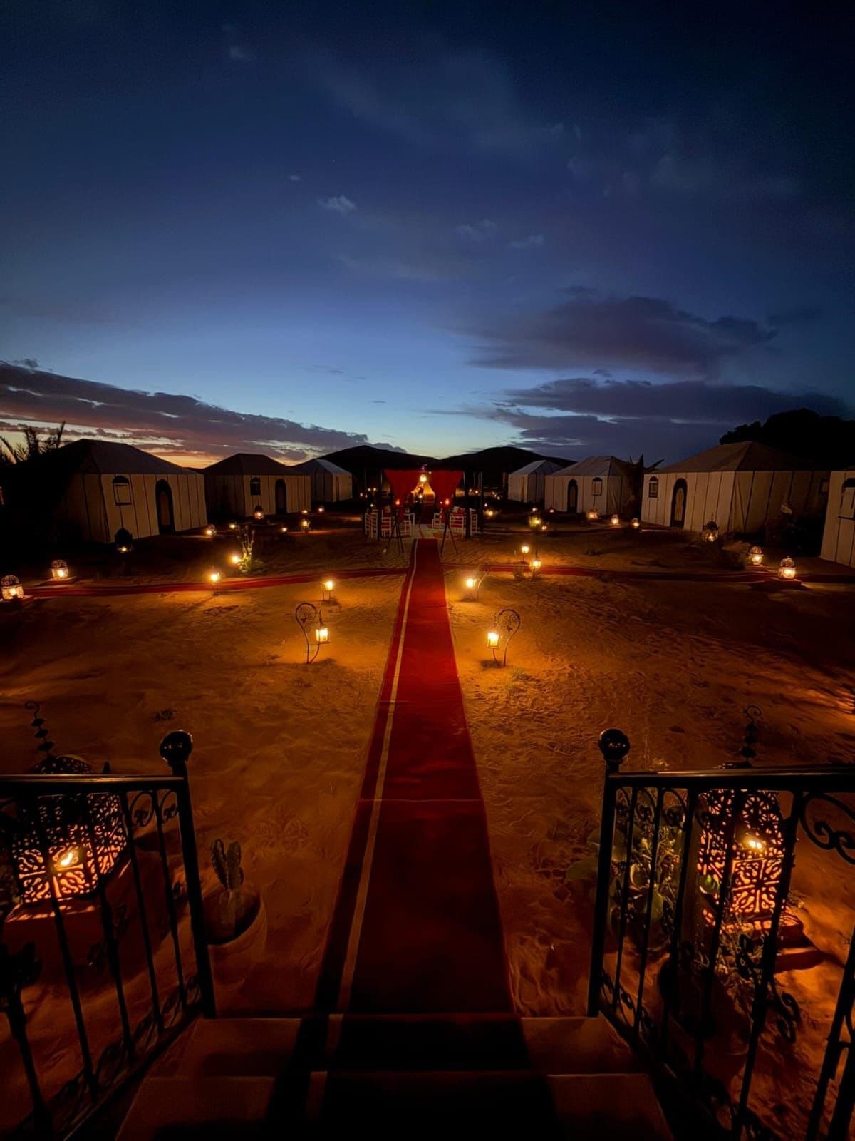 A desert camp at dusk, with lanterns along a runner between the tents